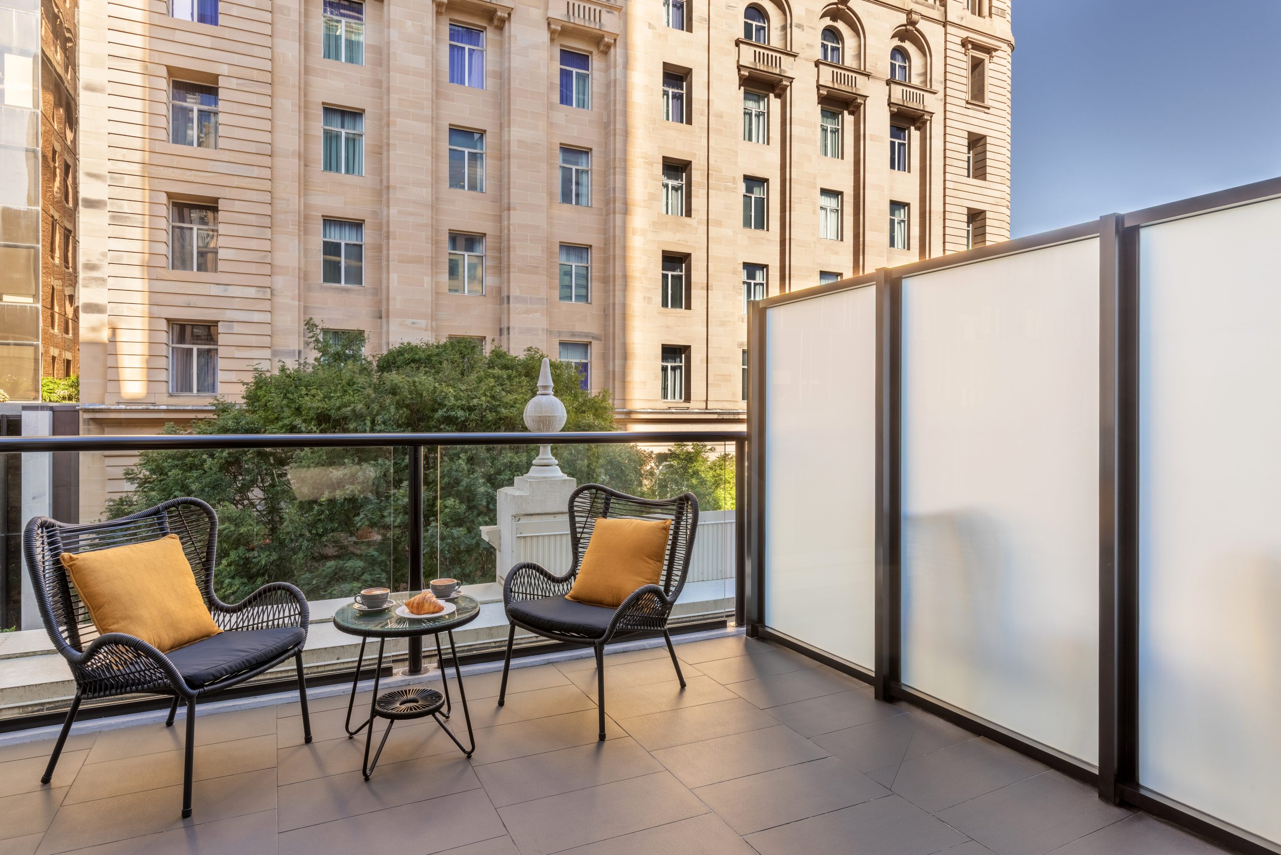 Image of two chairs on a balcony with a coffee and croissant in the middle on a table.