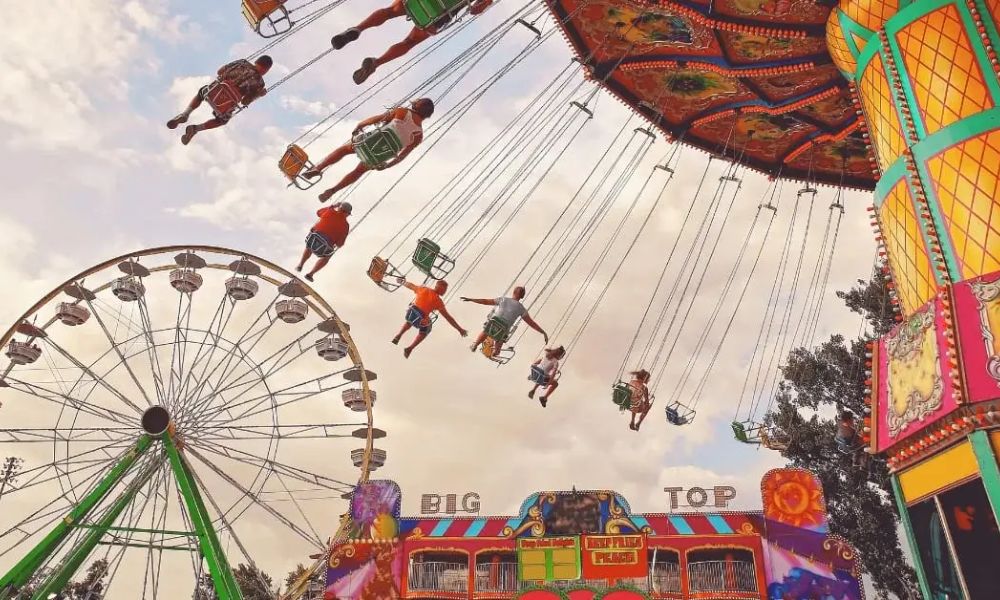 People having fun on a fairground ride and a ferris wheel in the background.