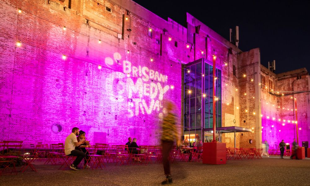 Exterior photo of Brisbane Powerhouse, lit up with projections of Brisbane Comedy Festival
